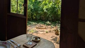 A dining table set with plates, cutlery, and a glass, with a window revealing a forested outdoor area.