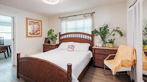 Ein Schlafzimmer mit einem hölzernen Bett, Nachttischen, einem Sessel und Topfpflanzen.