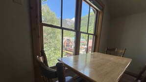 A dining area with a table and chairs, large windows with a view of trees and buildings, and a wooden door. - Ore Station 9: Hot Tub, Ski IN/OUT at Base of Gondola (Telluride)