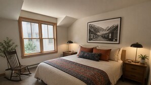 A bedroom with a large bed, a window, a framed picture, a rocking chair, and bedside tables. - Ore Station 9: Hot Tub, Ski IN/OUT at Base of Gondola (Telluride)