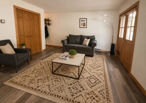 Una sala de estar con sofá, sillón, mesa de centro y alfombra estampada.