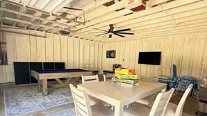 Ein Zimmer mit Holztisch, Stühlen, Deckenventilator und Dartscheibe.