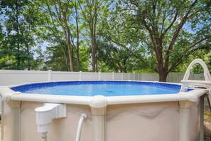 Una piscina elevada con cerco blanco y árboles al fondo.