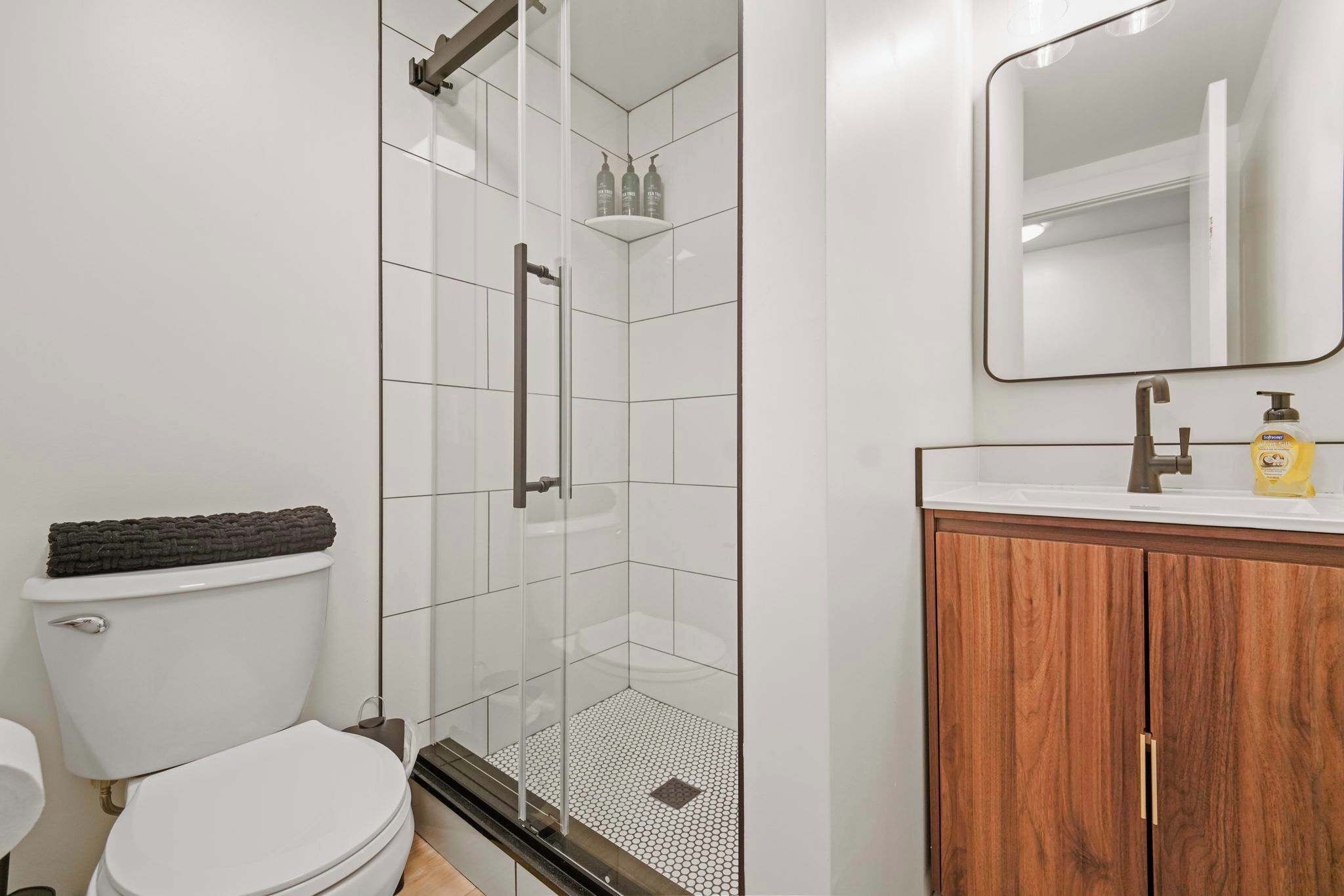 A bathroom with a glass-enclosed shower, a toilet, a sink with a wooden cabinet, and a mirror.