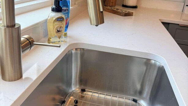 Ein Edelstahl-Spüle mit einem modernen Wasserhahn, einer Flasche Geschirrspülmittel und einem Messerblock auf der Arbeitsplatte.