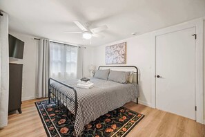 Un dormitori amb un llit, un ventilador de sostre, una porta i una finestra amb cortines.