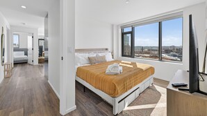 A modern hotel room with a large bed, a desk, a TV, and a city view. - 2-bedroom Boutique Suite in SoWa Boston (Boston)