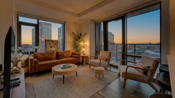 A modern living room with a sofa, armchairs, a coffee table, and a large window offering a city view. - 2-bedroom Boutique Suite in SoWa Boston (Boston)