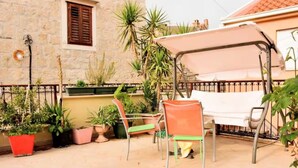 En udendørs terrasse med bord og stole, plantekasser og en bygning med stenvægge og et vindue.