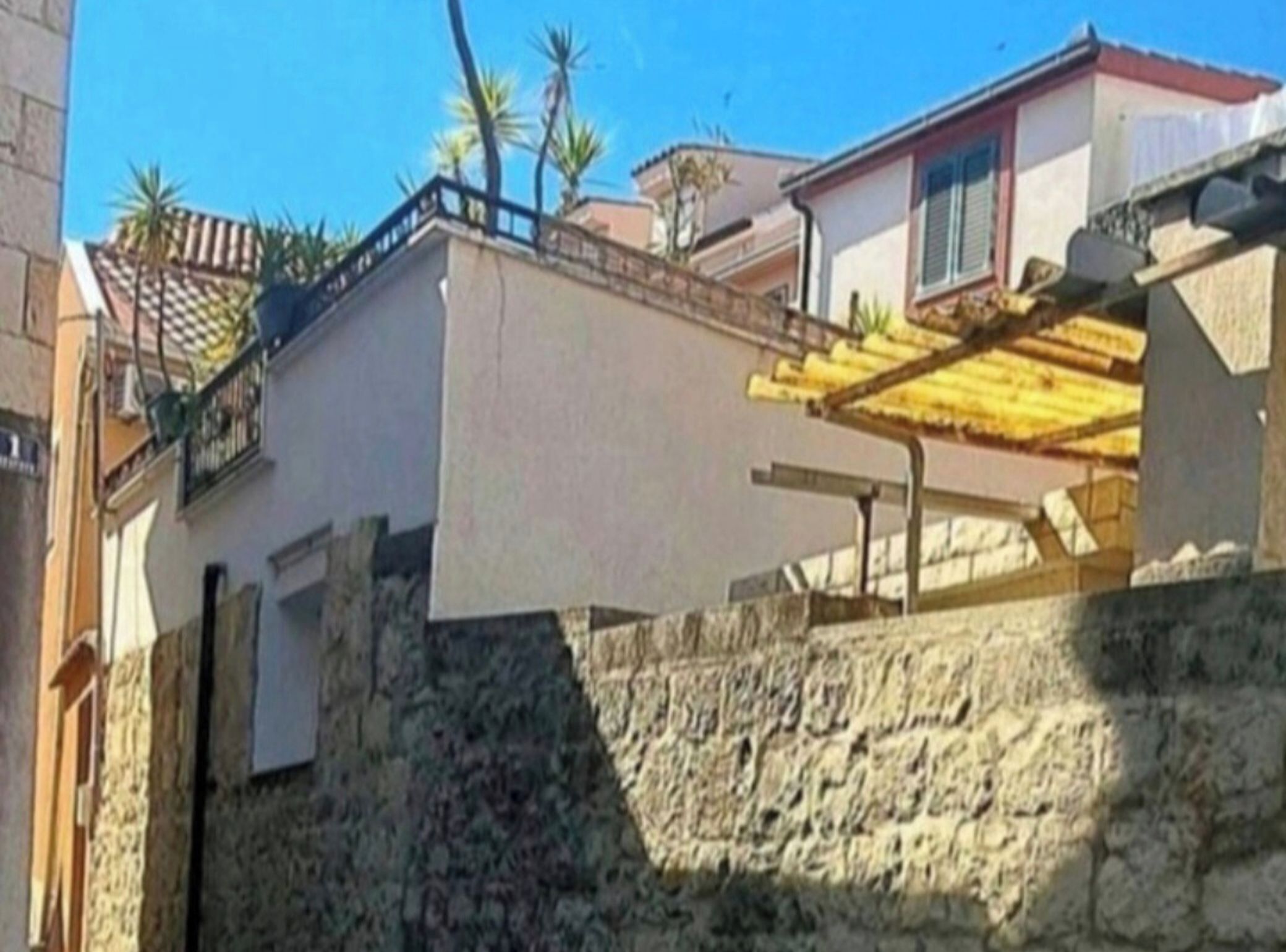 Edifício residencial com parede de pedra, varanda e telhado cerâmico.