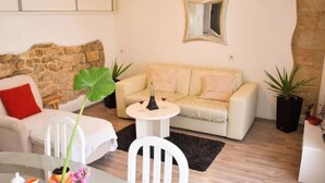 En stue med sofa, sofabord, stol, potteplante og et spejl på væggen.