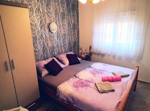 Une chambre à coucher comprenant un lit, une armoire, une lampe fixée au mur et une fenêtre avec des rideaux.