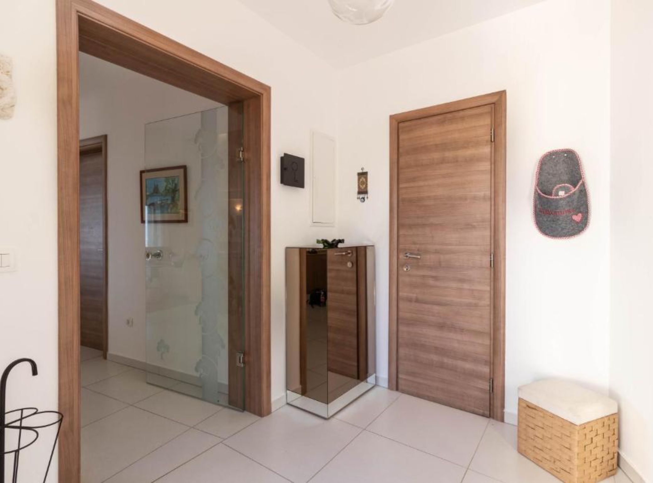 A hallway with a wooden door, a glass door leading to another room, and a small bench.