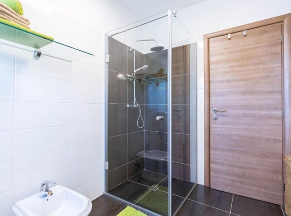 A bathroom with a glass-enclosed shower, a white sink, and a wooden door. - Villa Bella Sol (Lovran)