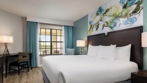 A hotel room with a large bed, a desk with a chair, a window with curtains, and a wall with a floral painting. - 2 bedroom condo at Holiday Inn Vacation Club Orange Lake Resort in Kissimmee, FL (Kissimmee)