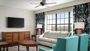 A living room with a sofa, teal armchairs, a wooden cabinet, a TV, and patterned curtains. - 2 bedroom condo at Holiday Inn Vacation Club Orange Lake Resort in Kissimmee, FL (Kissimmee)