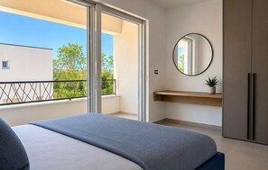Ein Schlafzimmer mit Bett, Spiegel, einer kleinen Pflanze und einem Balkon mit Geländer.