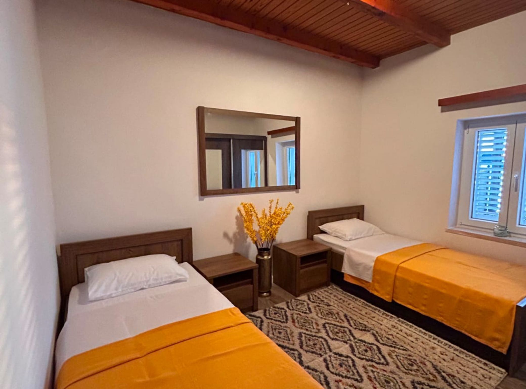 A hotel room with two beds, a mirror, a window with blinds, and a patterned rug.