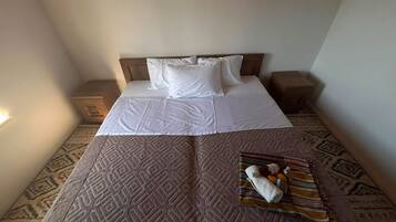 Een net opgemaakt bed met witte lakens en kussens, een kamerkleed met dessin, en een dienblad met handdoeken en toiletartikelen.