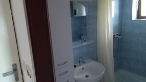 A bathroom with a white sink, a mirror, a shower, and a cabinet.