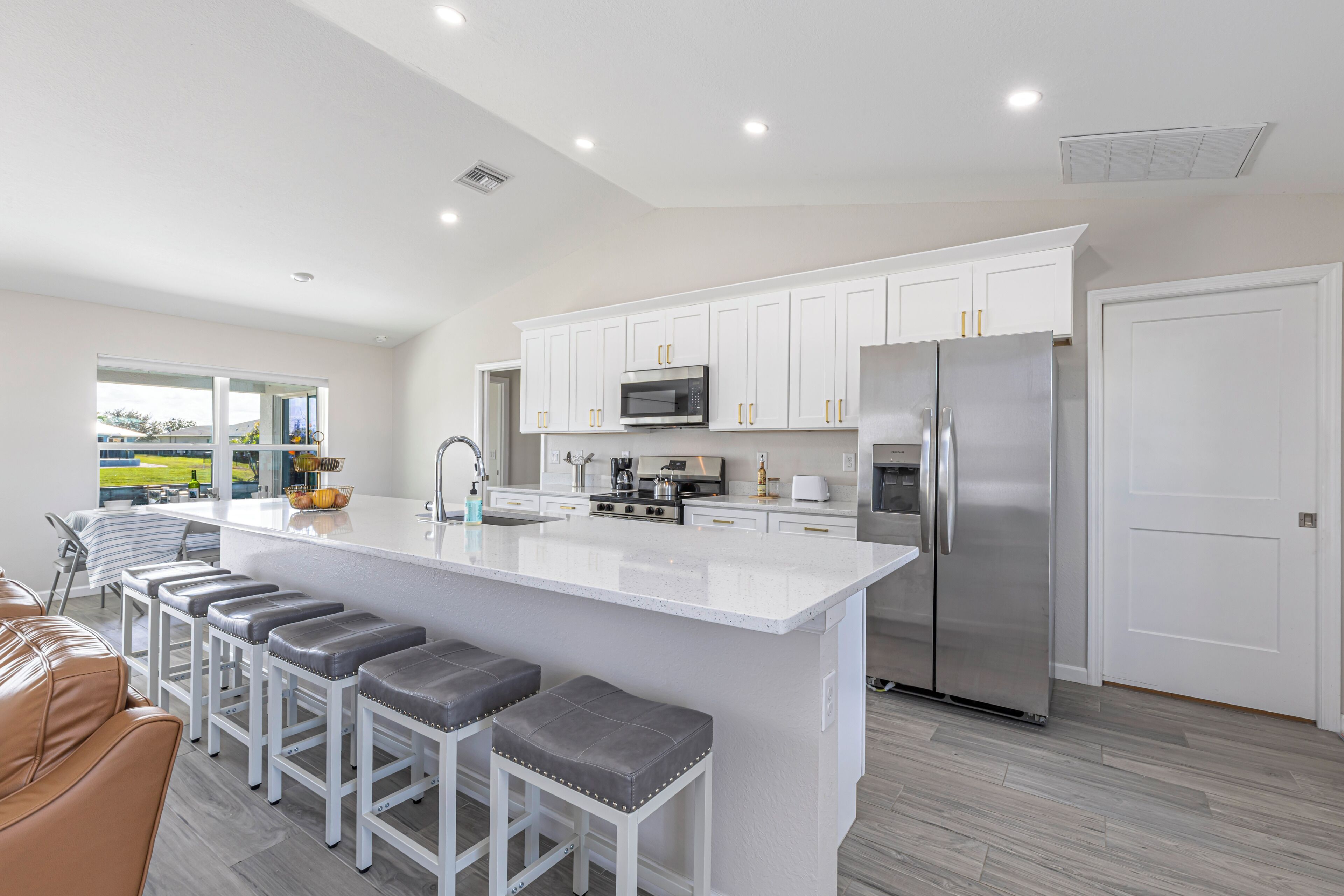 A modern kitchen with white cabinetry, stainless steel appliances, and a central island with bar stools.