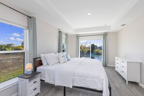 Ein Schlafzimmer mit einem großen Bett, einem Nachttisch mit Lampe, einer Kommode und einer Glastür, die auf einen Balkon führt.
