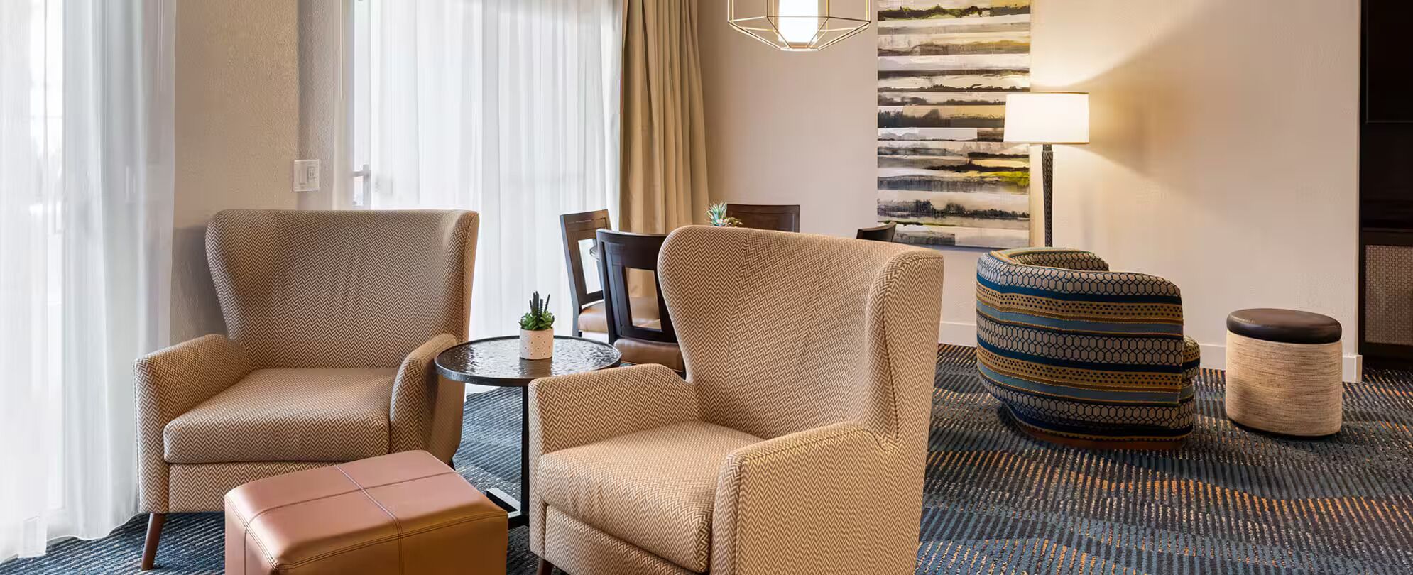A hotel room with a sofa set, a small table with a plant, a lamp, and a decorative wall piece.