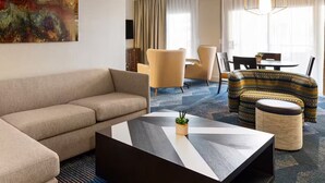 Ein modernes Hotelzimmer mit einem beigen Sofa, einem geometrischen Couchtisch und einem gemusterten Hocker.