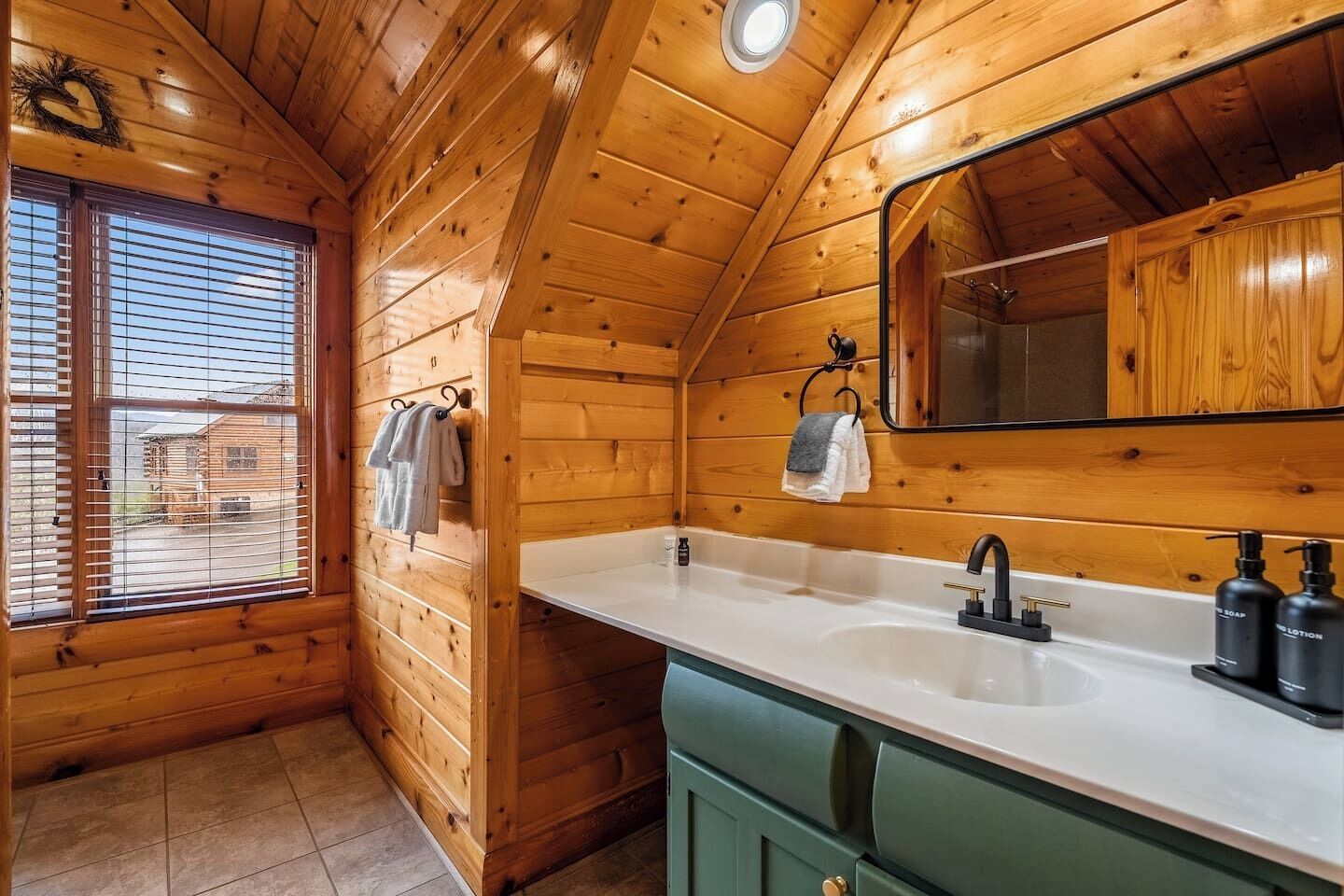 Interior de una cabaña de madera con baño que incluye lavamanos, espejo y armarios verdes.