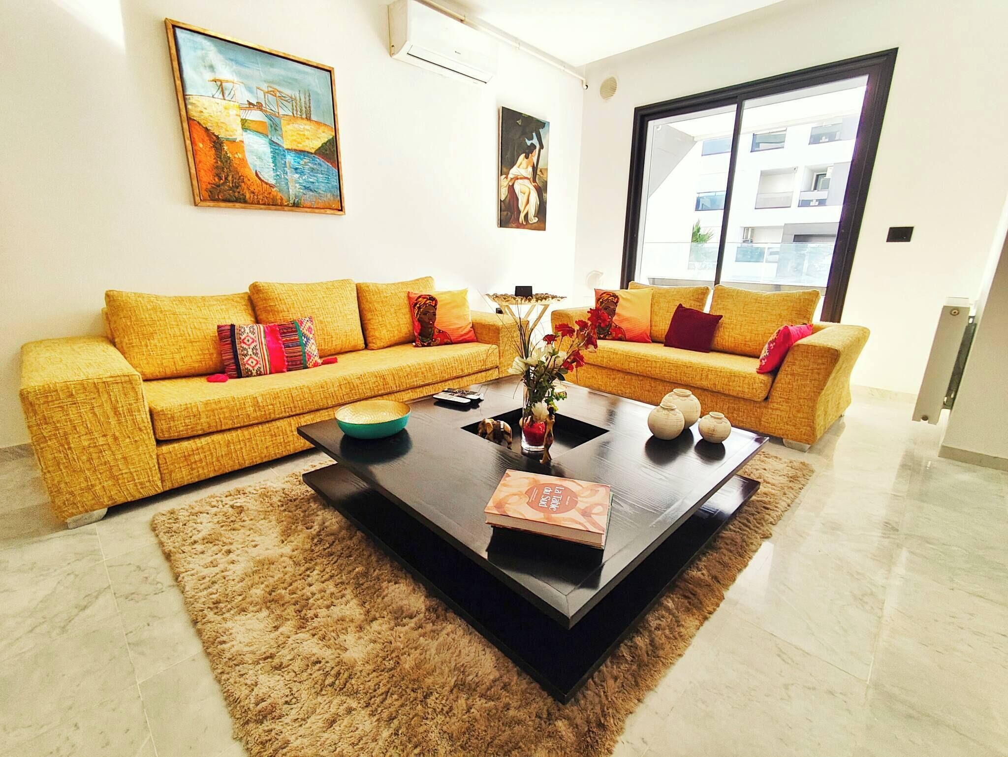 A living room with a yellow sofa set, a coffee table, and two paintings on the wall.