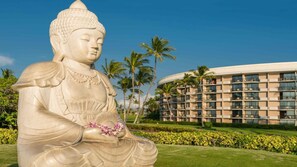 Una gran estatua de Buda en un jardín cuidado, con palmeras y un moderno edificio de hotel al fondo.