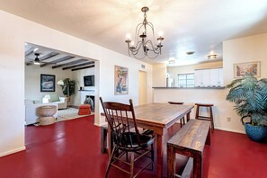 A dining area with a wooden table and chairs, a chandelier, and a red floor. - 3BR Near Hospitals & UofA w/ Workspace (Tucson)