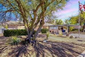 A building with a covered outdoor area, a flag, and a tree. - 3BR Near Hospitals & UofA w/ Workspace (Tucson)