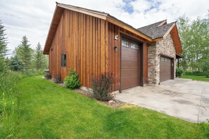 A two-story wooden house with a stone facade, a garage, and a well-maintained lawn.
