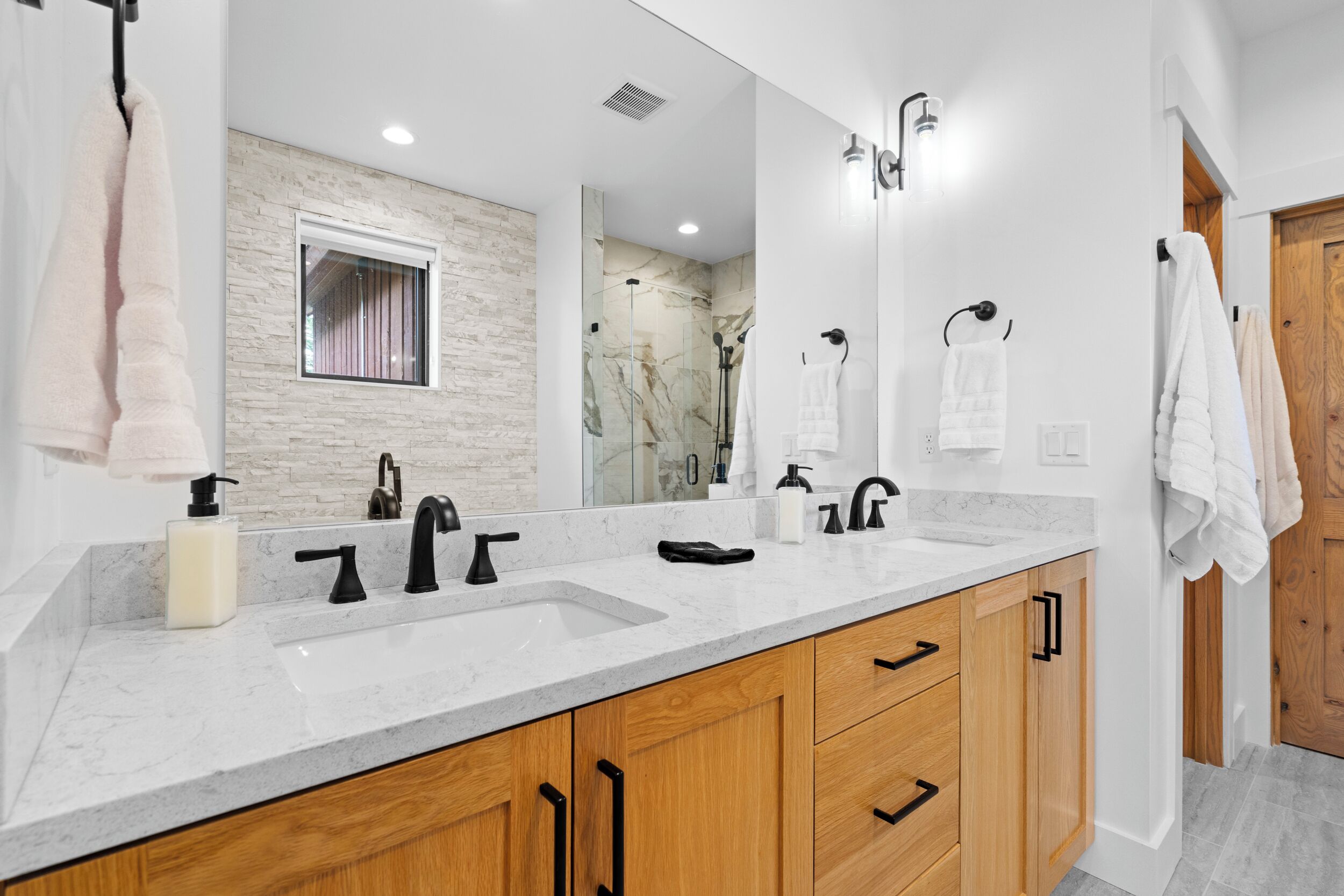 Un baño moderno con un espejo grande, dos lavamanos, una ducha y armarios de madera.