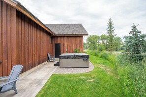 A wooden building with a patio area, a hot tub, and a chair.