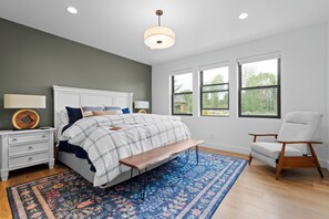Ein Schlafzimmer mit Bett, Nachttischen, einer Bank, einem Sessel und großen Fenstern.
