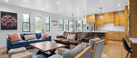 A modern living room with a sofa, chairs, a coffee table, and a kitchen area with wooden cabinets and a refrigerator.