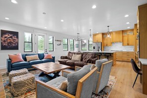 A modern living room with a sofa, chairs, a coffee table, and a kitchen area with wooden cabinets and a refrigerator.