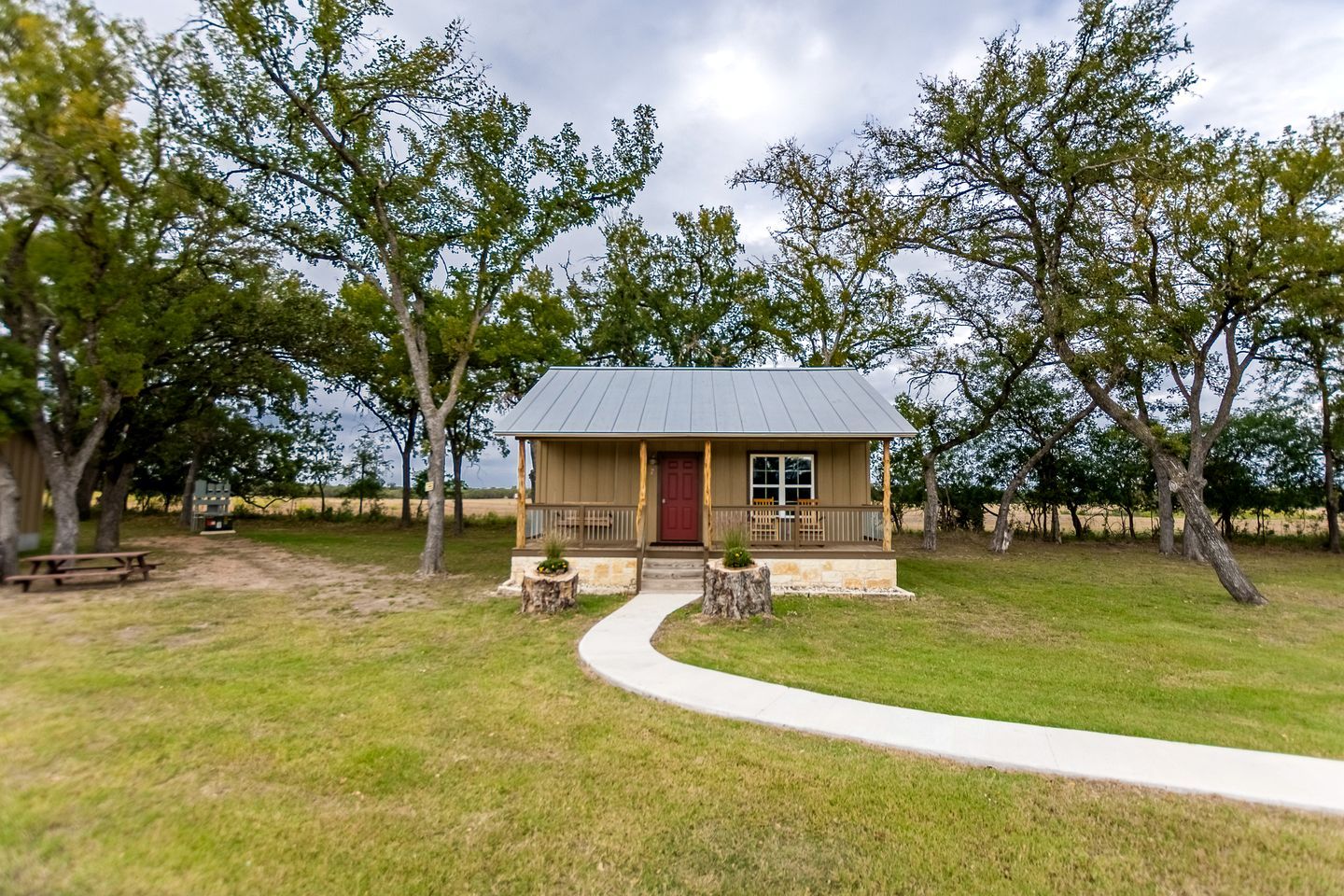 A small cabin with a porch, surrounded by trees and a grassy area.