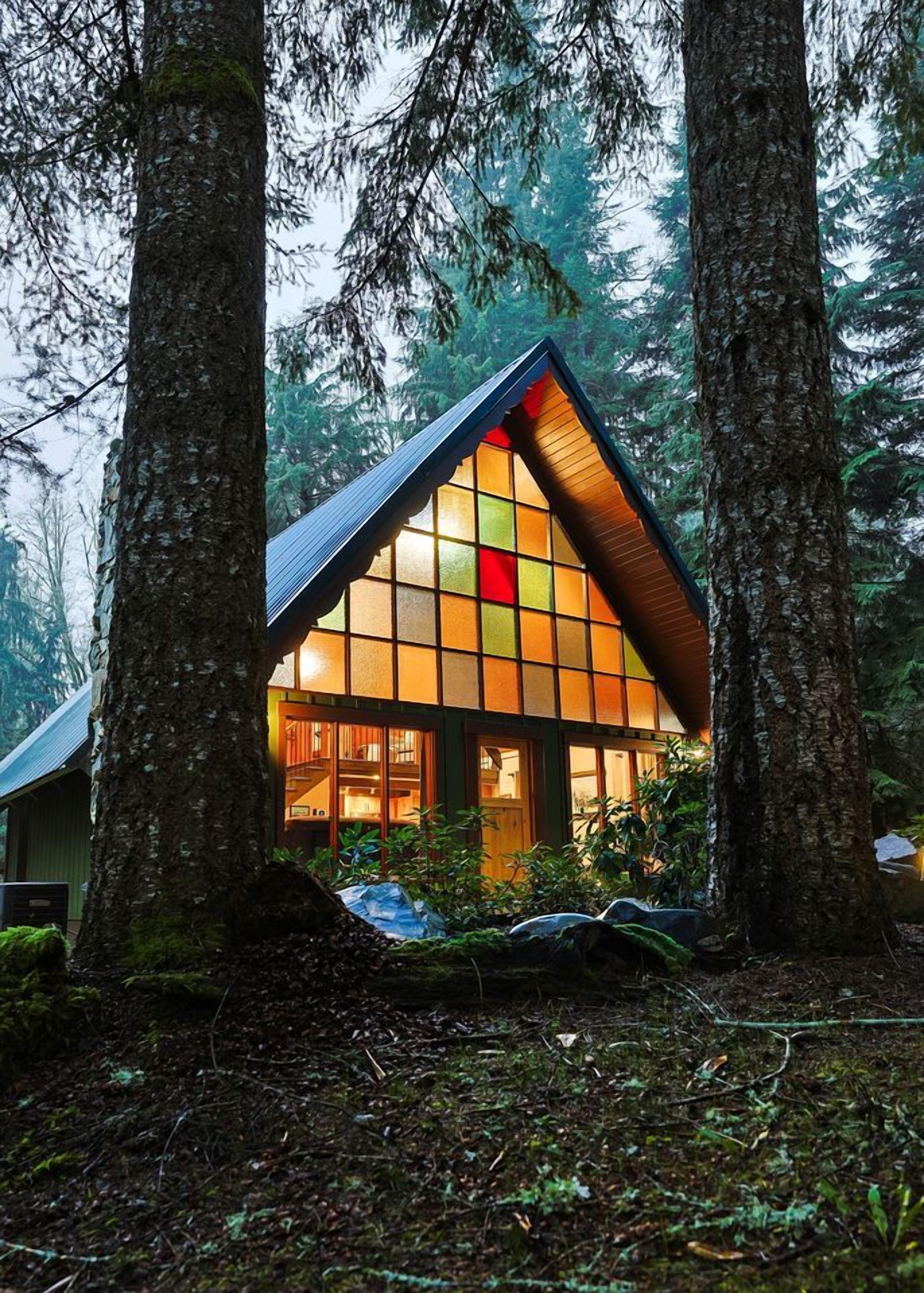 Une cabane dotée d’un toit triangulaire, entourée de grands arbres.