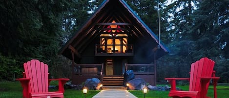 Une cabane avec un foyer et deux chaises Adirondack rouges devant.