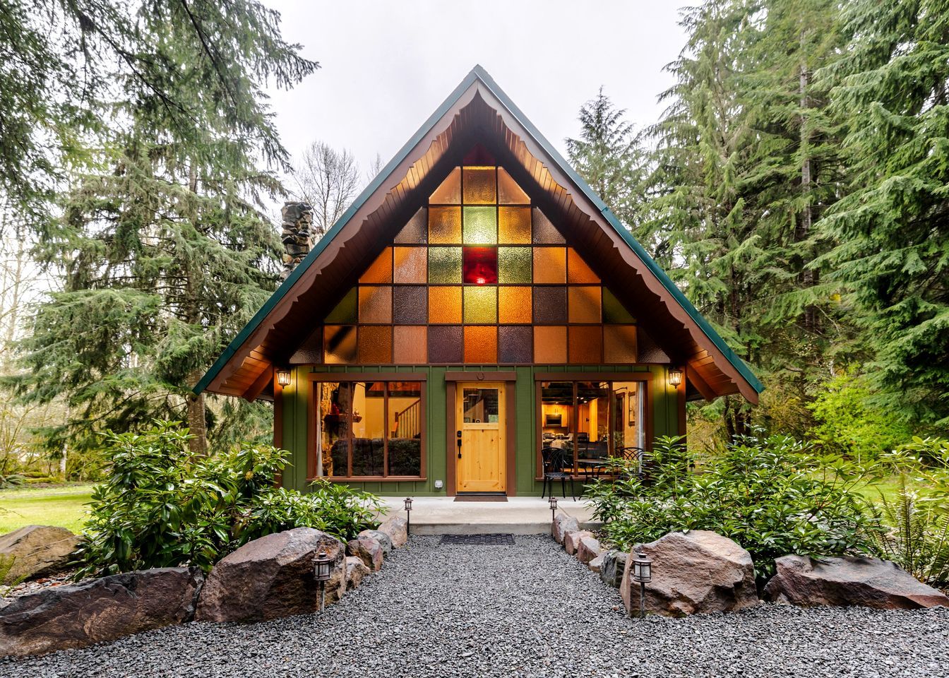 A cabin with a triangular roof, large windows, and a gravel driveway.