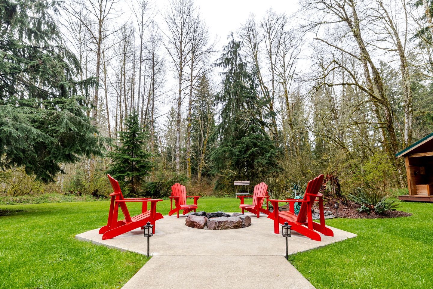 Un área de patio con sillas Adirondack rojas, un brasero y una cabaña de madera al fondo.