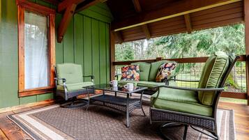 A covered porch with green walls, a wicker table, two chairs, and a sofa with colorful cushions.