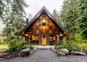 Una cabaña con techo triangular, ventanas amplias y un camino de entrada de grava.