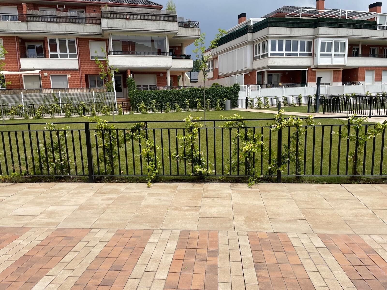 En boligbygning med flere altaner, en anlagt sti og et hegn med beplantning.