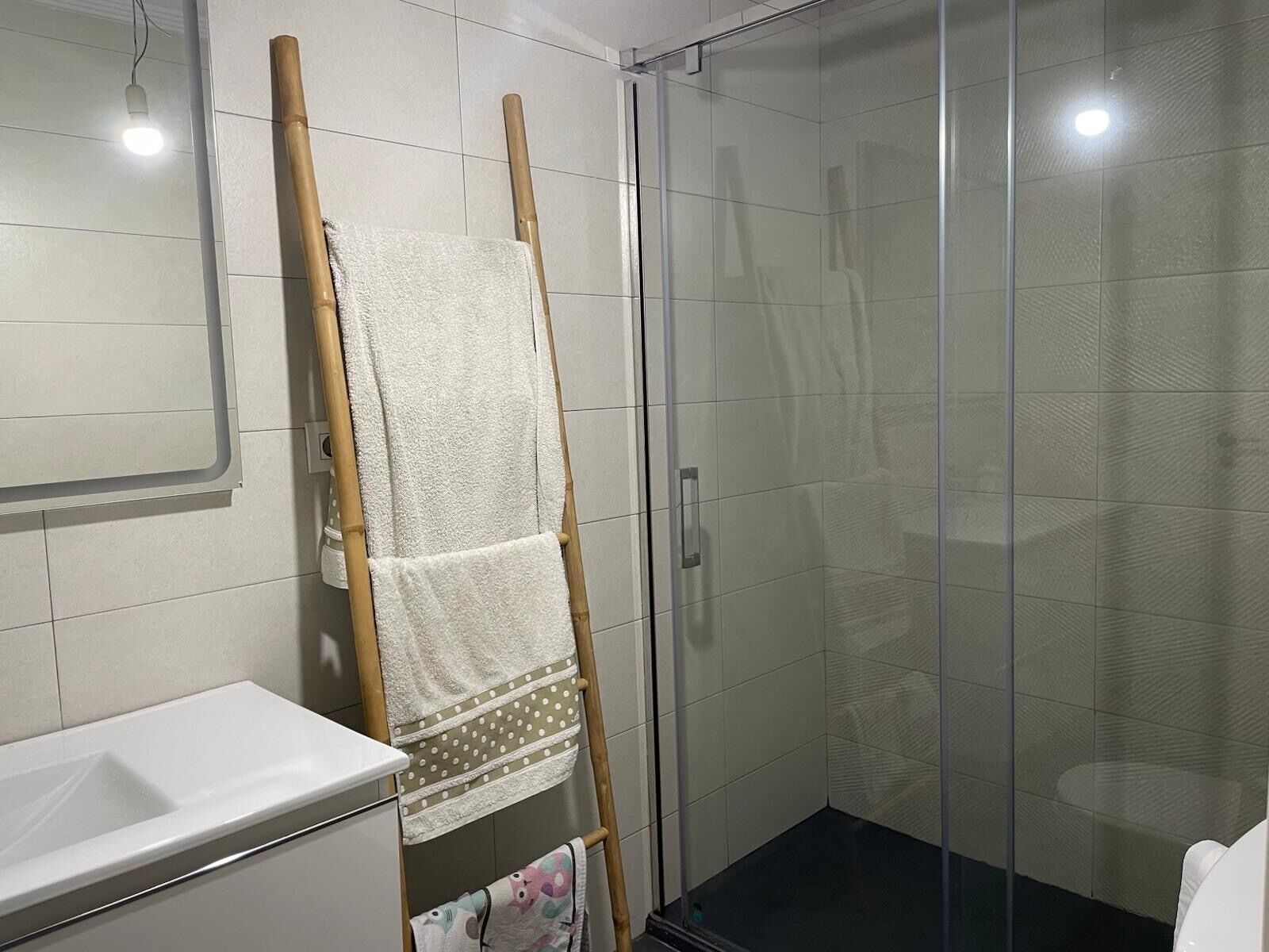 Un bagno con box doccia in vetro, un lavandino bianco e un portasciugamani con diversi asciugamani.