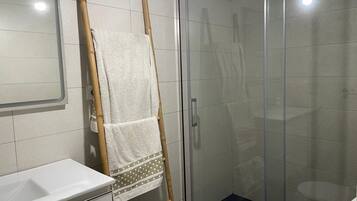 Een badkamer met een douchecabine van glas, een witte wastafel en een handdoekrek met meerdere handdoeken.