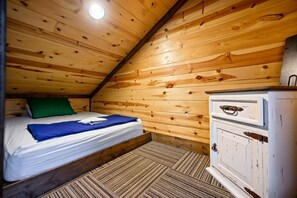 Une pièce de cabane en bois comprenant un lit, une commode et un plafond en pente.